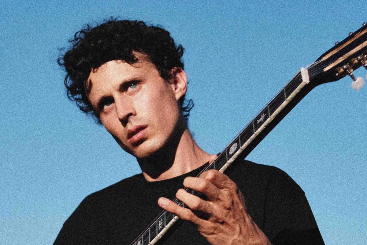 Le chanteur Paul Barreyre jouant de la guitare sur un fond bleu ciel.