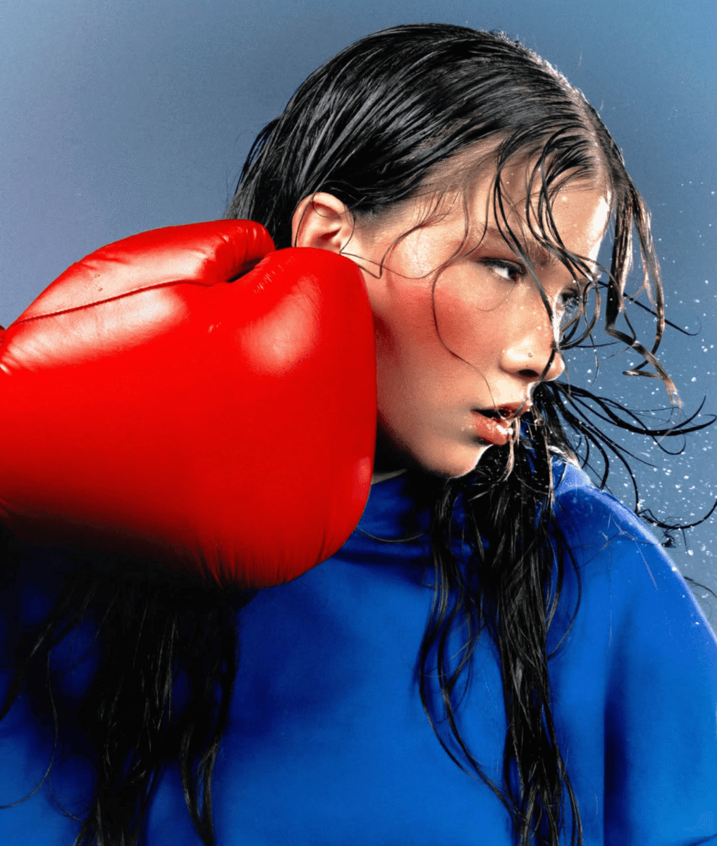 Pochette du titre Nulle de Marie Jay, extrait de l’EP Le rose c’est hasbeen Marie Jay habillée en bleu reçoit un coup de poing avec un gant de boxe rouge sur la pochette du morceau Nulle.